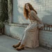 A young woman wearing a 1970s outfit standing next to a white brick wall