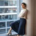 A woman wearing a navy pleated midi skirt paired with a cream-colored sweater and sleek ankle boots for a casual business outfit.